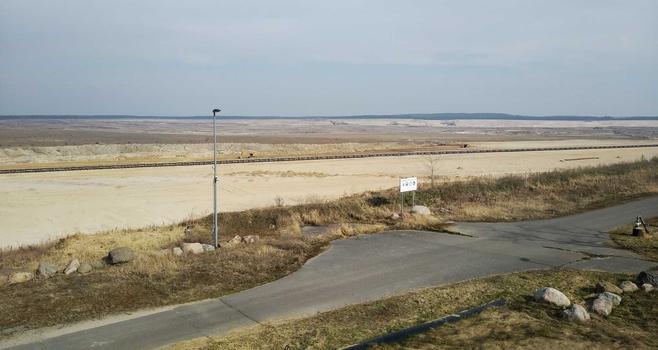 Blick über den Tagebau Jänschwalde bei Griesen. vorne führt ein Weg mit Straßenlampe vorbei, dahinter abgebaggerte Flächen, in der Ferne riesige Schaufelradbaggger.