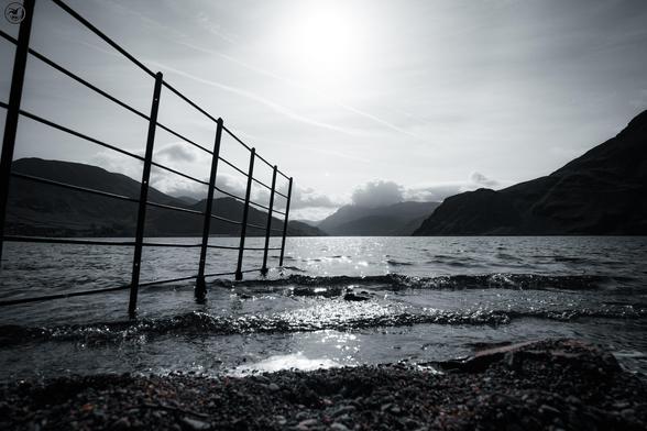monochrome shot of lake waters with metal fence stretching out into the water.