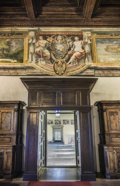 An historic ornate wood framed door with an elaborate fresco above. Through the door is seen a brightly lit outer room.
