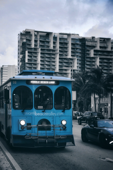 Miami beach trolley in the street with large apartment buildings, palm trees and expensive cars passing.