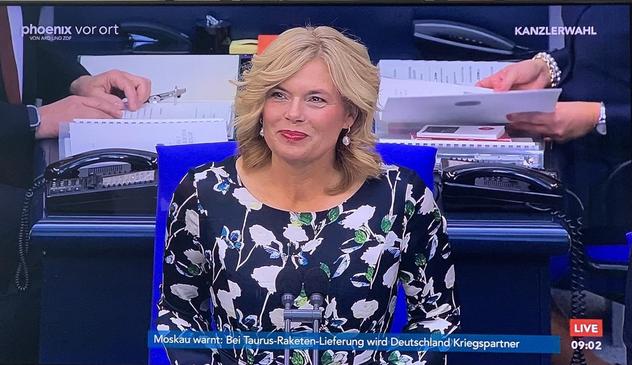 Julia Klöckner mit frisch blondierten Haaren, die ein schwarz-weißes Blumenkleid trägt, spricht auf dem Podium des Bundestags.