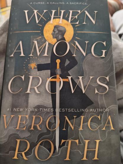Cover of When Among Crows by Veronica Roth. Cover is a blue grey color with a man standing with a sword at his side. The sun is behind him.