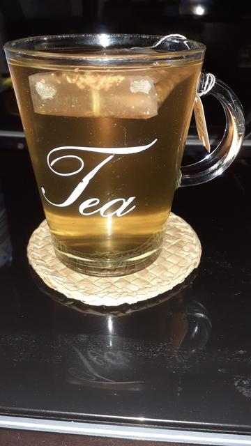 Ein konisches Teeglas gefüllt mit gelb farbenen Tee in Nahaufnahme auf einem dunkel braunen Couchtisch.