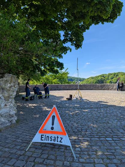Ein "Einsatz"-Warnschild vor einer Analogantenne unterhalb der Sparrenburg. 3 THW Helfer:innen neben der Antenne und koordinieren Funksprüche mit den Einsatzfahrzeugen.