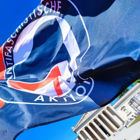 Foto: Die Flagge der ANTIFASCHISTISCHEN AKTION weht über dem Königsplatz, im Hintergrund die Glyptothek.
Alles unter wolkenlosem Himmel.