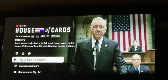 A picture of a TV showing the House of Cards screen on Netflix featuring the description title, the selected episode of season op1 episode 7 and on the right of the screen is Spacey standing at a microphone with what appears to be the floor of Congress and Dias with the House Speaker behind him.