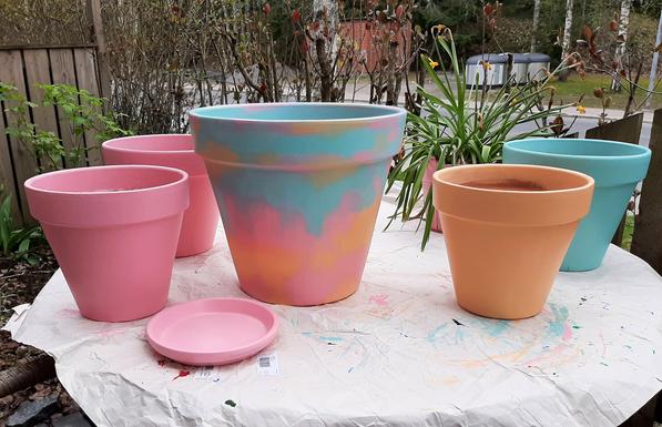 5 clay pots on a table paintef with light pastel colours, pink, blue, orange.