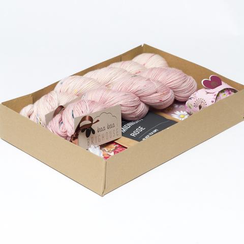 Picture shows an open A4 box containing two skeins of yarn in shades of pink with red, yellow and blue speckles. The rest of the box contents are obscured by the sides.