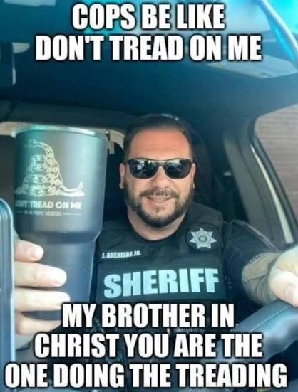 A photo of a man in a car wearing sunglasses. He is wearing what looks like a bulletproof vest with the word Sheriff on it and a sheriff's badge. He is holding a thermos with the "Don't Tread on Me logo on it.

There is also text overtop this image which reads, "Cops be like Don't Tread On Me. My brother in Christ, you are the one doing the treading"