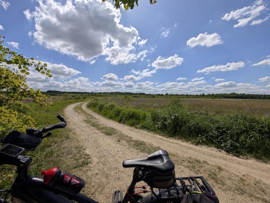 Blick über die Querwind Einflugschneise in der Wahner Heide. Der Himmel blau mit Schönwetterwolken.
Unten, angeschnitten, mein Pedelec.