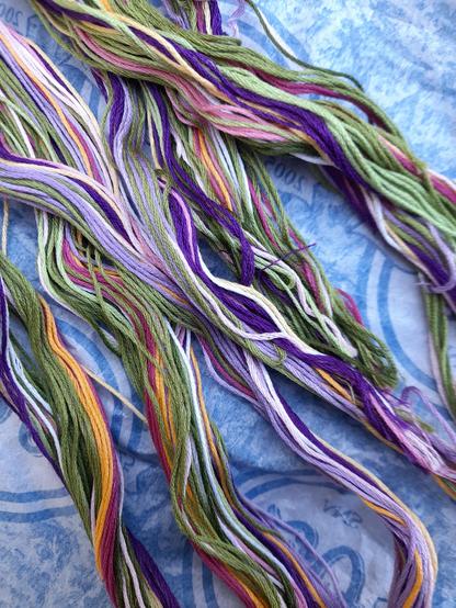 Strands of embroidery thread in mixed colours, mainly shades of green and purple.