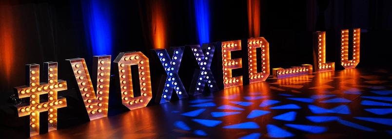 La scène des Voxxed Days Lux avec en fond le hashtag voxxed_lu réalisé avec une enseigne lumineuse.