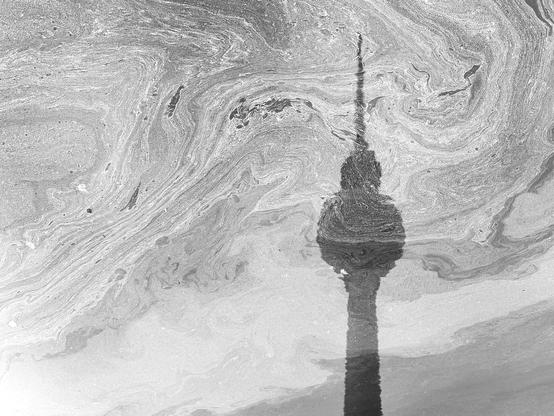 Abstract black and white image of swirling patterns resembling liquid, with the silhouette of a tower reflected in the surface.