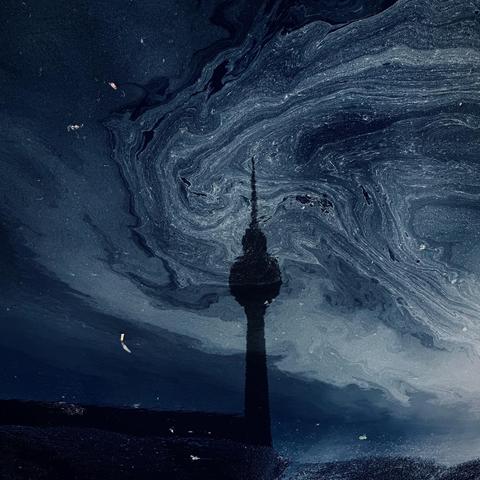 A dark, swirling pattern in a body of water reflects the silhouette of a tall tower, creating an abstract and moody composition.