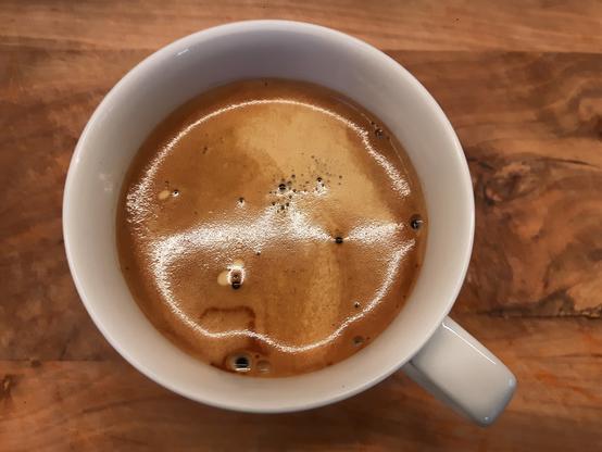 Eine Tasse Americano steht auf einem Holzbrett.