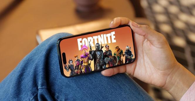 Eine Person hält ein iPhone in der Hand, auf dem der Startbildschirm des Spiels Fortnite zu sehen ist.