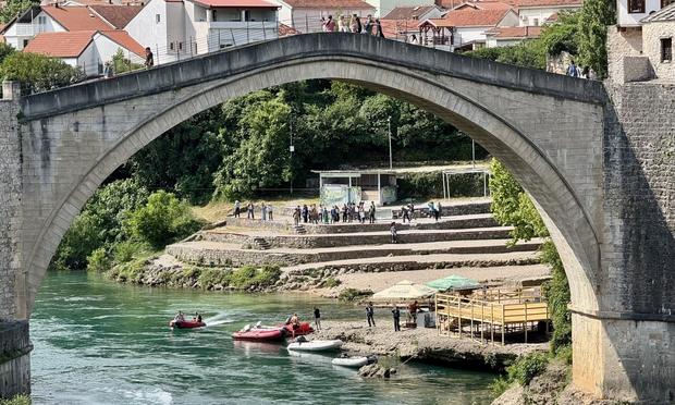 People cross Old Bridge in Mostar; boats on river below