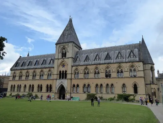 The image shows a large, historic building with Gothic architectural features, including pointed arches and detailed stonework. It has a tall spire and is set in a grassy area with people walking around. The sky is partly cloudy. This building appears to be a museum or educational facility, likely situated in a university or cultural context.

Image Credits: Wikimedia / Ethan Doyle White / CC BY-SA 4.0