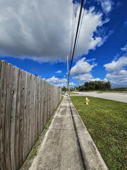Long, straight section of pedestrian sidewalk next to an old wooden fence.