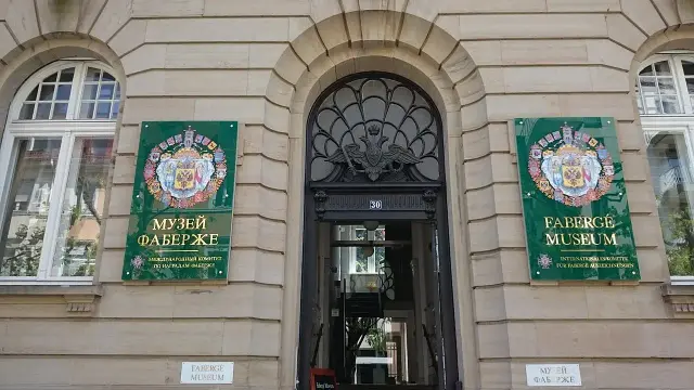 The image depicts the entrance of the Fabergé Museum. There are two large green banners on either side of the door, with text identifying the museum in both Russian and English. The building features decorative architecture above the entrance, contributing to its historical appearance.

Image Credits: Wikimedia / Klaus Graf / CC BY-SA 3.0