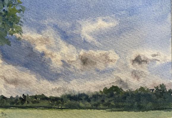 A band of trees stretches across the horizon beneath a wide expanse of sky, where large, drifting clouds curl and stretch in sweeping shapes that suggest a quiet, open afternoon.