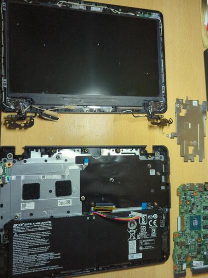 Auf einer Arbeitsfläche liegt ein zerlegter Asus-Netbook B117 
Deutlich erkennbar Deckel ohne Rahmen mit Display und den beiden Scharnieren, sowie das Unterteil aus dem die Platine, Kühlableitblech und diverser Kleinkram rausgeklst wurde und nur noch der Akku an seiner Stelle ist.