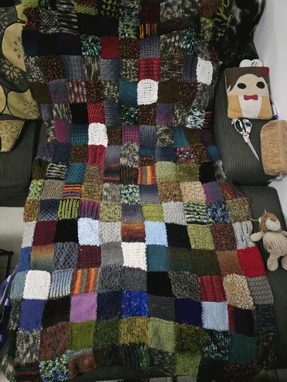 A knitted patchwork blanket with a lot of different squares in mainly earthy autumnal tones, and with different textures and stitches.