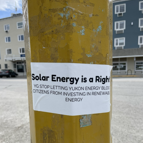 A printed sticker is mounted on a lamppost. It reads, “Solar energy is a right. YG stop letting Yukon Energy block citizens from investing in renewable energy.”