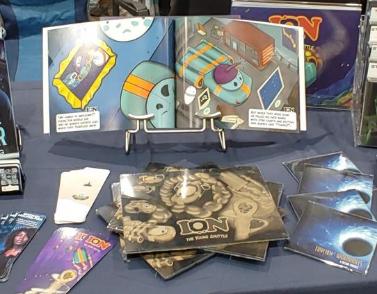 Convention table set up with books, bookmarks, and associated art for sale