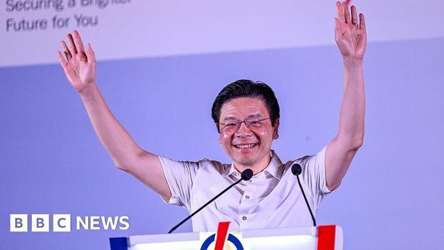 Singapore PM Lawrence Wong smiles with both his arms held aloft as he addresses a crowd at an election rally