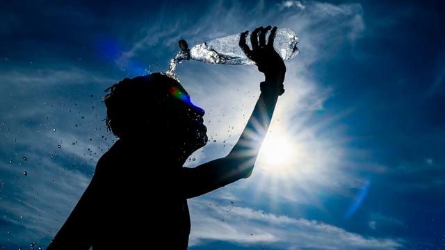A person pouring water over their head in the heat of the sun. | Frederic Sierakowski/EPA-EFE