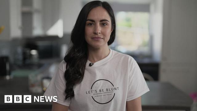 Leanne Lucas, who has long dark hair, smiles at the camera while wearing a white t-shirt with the logo 'Let's Be Blunt - Remove the Point'