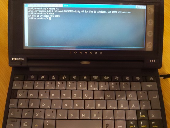 A badly lit photo of a HP Jornada 680 running a brand-spanking-new linux kernel, running dwm with a single terminal window, the terminal shows the output of "uname -a"and "date" showing us "Linux jornada6xx 6.8.0-rc3-next-20240209" and "Sun Feb 11 20:29:39 UTC 2024" respectively 