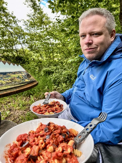Mann mit blauer Regenjacke isst Pasta mit Tomatensauce