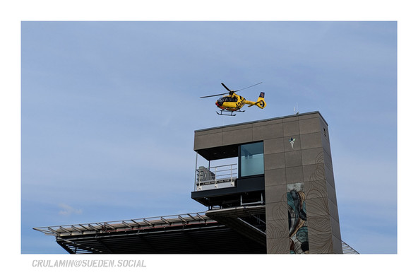 Ein gelber ADAC Rettungshubschrauber steigt von einem erhöhten Landepad mit angeschlossenem Gebäude auf.