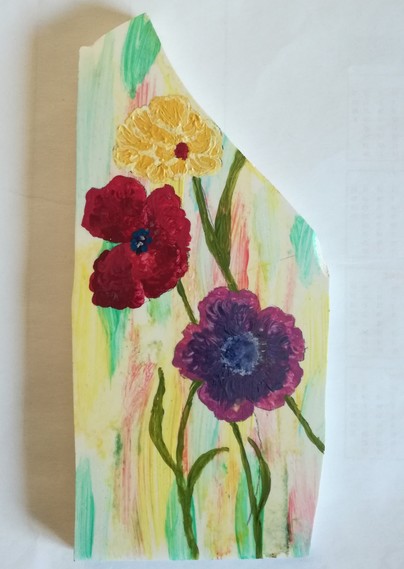 Drei Blüten, rot, gelb und violett auf einem Stück Fliese, das farbig grundiert ist.