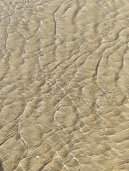 Kleinste Wellen reflektieren das Licht und erzeugen Muster im seichten Sand