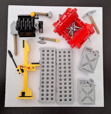 Das Bild zeigt eine Anordnung von Lego-Bausteinen auf einem weißen Hintergrund. Zu sehen sind ein schwarzer Motorblock, ein roter Kasten mit silbernen Werkzeugen darin, eine gelbe Konstruktion mit einem schwarzen Griff, zwei graue Gitterplatten mit Löchern sowie zwei graue Kanister mit einem X-Muster. Diverse Werkzeuge wie Hämmer und eine Axt liegen ebenfalls herum. Die Lego-Bausteine sind ordentlich auf dem weißen Untergrund angeordnet.