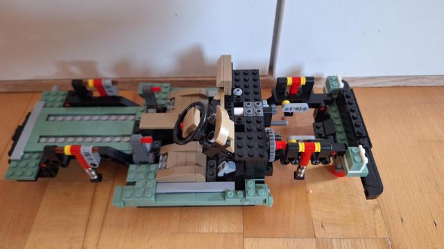 Das Bild zeigt ein unvollständiges Modell eines Lego-Autos. Das Chassis ist größtenteils aus grünen, schwarzen und beigen Legosteinen zusammengesetzt. Man kann das Lenkrad, die Sitze und die Aufhängung erkennen. Das Modell steht auf einem hellbraunen Holzboden. Im Hintergrund sind eine weiße Wand und eine hellbraune Fußleiste zu sehen.

Bereitgestellt von @altbot, generiert mit Gemini
