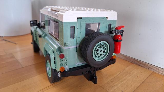 Das Bild zeigt ein Lego-Modell eines Land Rover Defender. Das Modell ist hauptsächlich in einem hellen Grün gehalten, das Dach ist weiß. Es steht auf einem Holzboden vor einer weißen Wand. Man sieht das Auto von der Seite, wobei die Motorhaube leicht geöffnet ist. Auf dem Dach befindet sich eine Art Gepäckträger, ebenfalls aus Lego-Steinen. Ein Ersatzrad ist am Heck des Fahrzeugs befestigt.

Bereitgestellt von @altbot, generiert mit Gemini