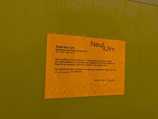 Aufkleber der Stadt Neu-Ulm auf einem Altkleidercontainer, der zur Entfernung des unrechtmäßig aufgestellten Containers auffordert 