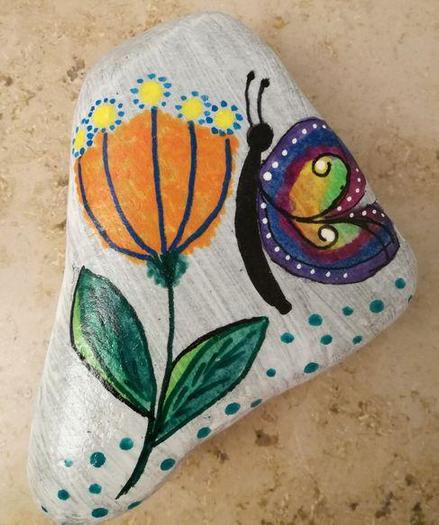 Eine Blume, bestehend aus zwei grünen Blättern, einem orangefarbenen Kopf, mit gelben Tupfen oben, die wiederum von blauen Punkten umgeben sind.
Daneben ein Schmetterling mit schwarzem Körper und bunten Flügeln.
Mit Acryl auf Stein gemalt.