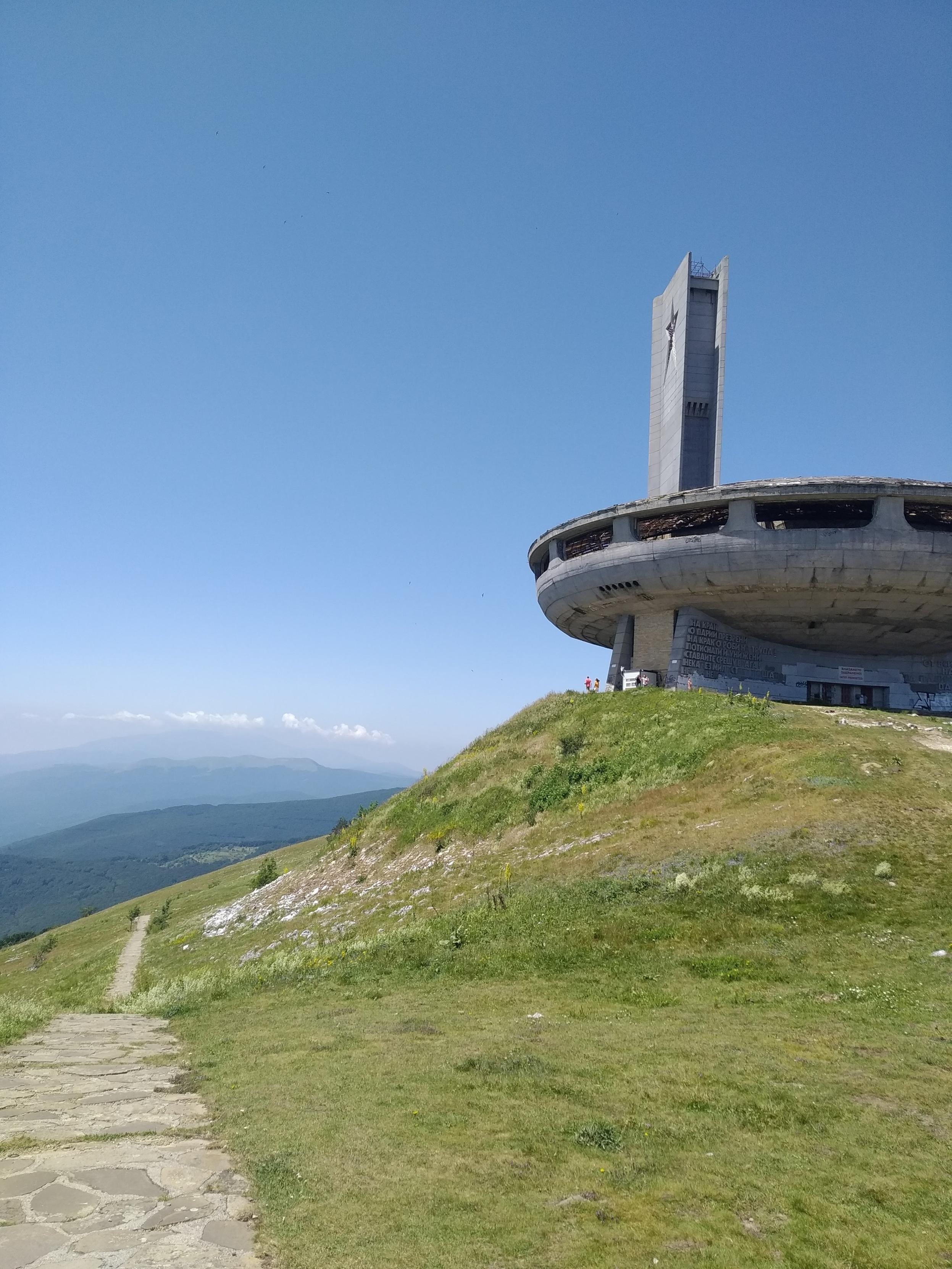 Auf einem grasgrünen Berggipfel des Balkangebirges steht eine steinerne fliegende Untertasse mit Turm Auf einem grasgrünen Berggipfel des Balkangebirges steht eine steinerne fliegende Untertasse mit Turm