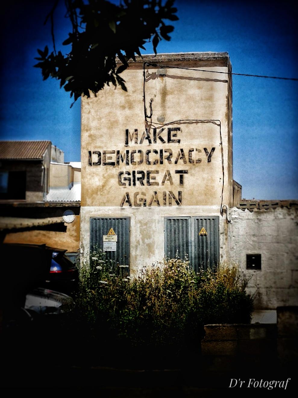 "Make Democracy great again" steht als schwarzes Schrift-Graffiti in Blockbuchstaben an einer Wand eines Transformatorgebäudes in Petra auf Mallorca