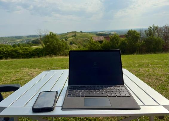 Laptop und Handy auf einem Campingtisch vor einer hügeligen Landschaft 