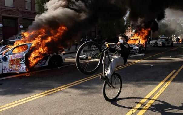 A demonstrator wearing a surgical mask does a wheelie in front of burning Waymo vehicles as protesters clash with law enforcement near the federal building during a protest in response to federal immigration operations in Los Angeles, on June 8, 2025.  
(Etienne Laurent, AFP via Getty Images)