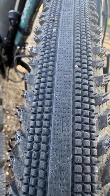 Nahaufnahme eines Mountainbike-Reifens mit Laufstreifenmustern. Der Reifen scheint mit sichtbarem Schmutz und Schmutz abgenutzt zu sein.

Das Bild zeigt den vorderen Reifen. 