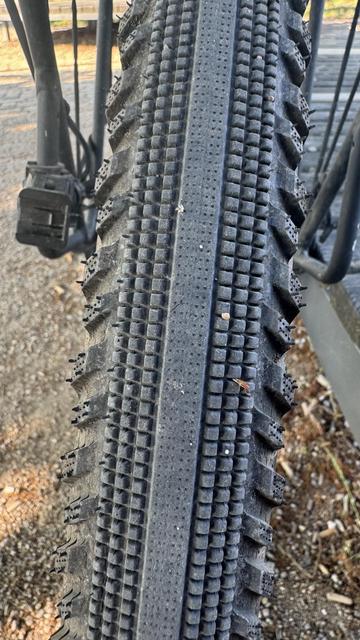 Nahaufnahme eines Fahrradreifens, der das Laufflächenmuster zeigt, das eine Mischung aus kleinen Knöpfen und flachen Abschnitten aufweist, was auf ein für verschiedene Gelände geeignetes Design hinweist. Das Bild erfasst Schmutz und Schmutz auf der Reifenoberfläche.

Das Bild zeigt den hinteren Reifen. 