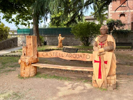 Eine aus Holz gefertigte Sitzbank mit einer Ritterfigur und einem Turm, jeweils aus einem Baum geschnitzt 