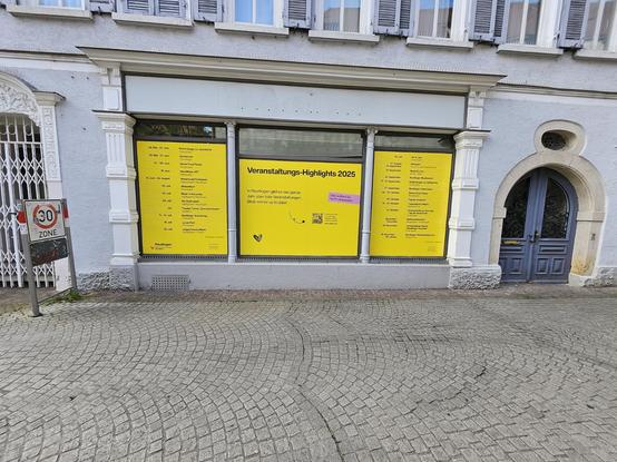 Foto vom Schaufensters des ehemaligen Breuningergeschäfts in Re. Das Schaufenster ist mit einem gelben Plakat beklebt. Dies zeigt die Veranstaltung im Sommer in Reutlingen.